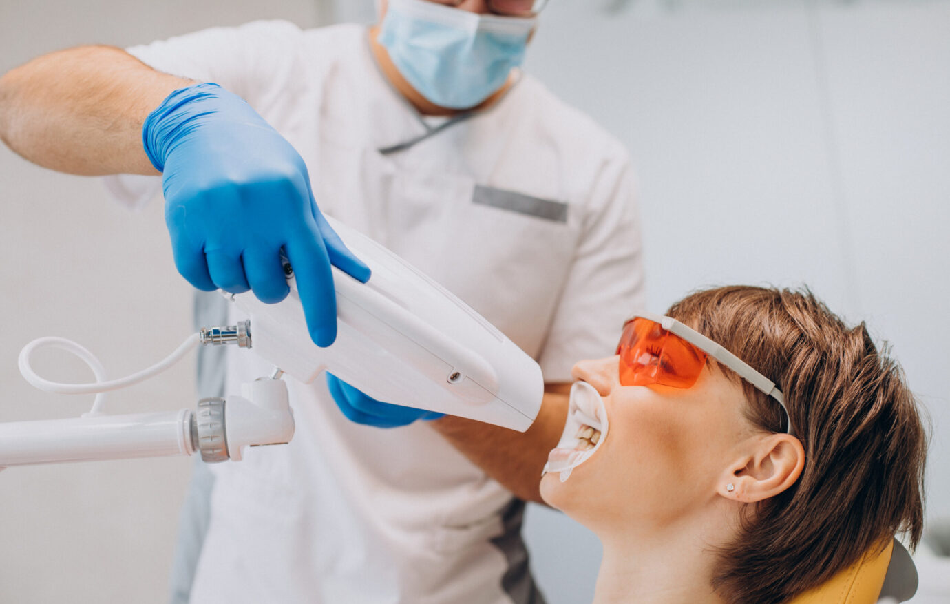 Woman whitening teeth at dentistry with special equipment
